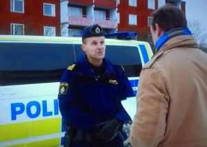 En representant för media i samspråk med en polis. Vi kallar honom Tomas. Detta är en miljö/situationsbild. Tomas har inte nödvändigtvis någon direkt koppling till avrättningen i Husby.